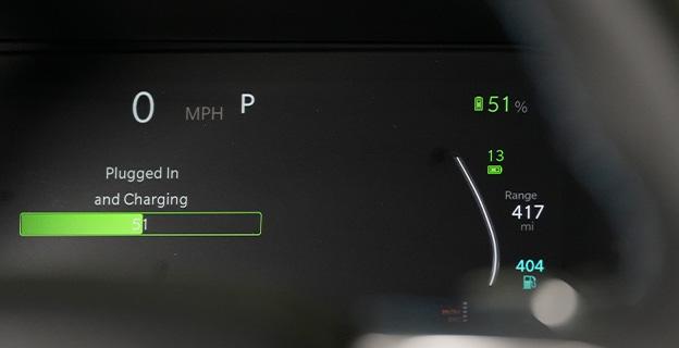 Electric vehicle dashboard status for plugged in and charging displayed along with battery percentage and range levels.