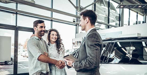 A couple shakes hands with a salesperson in a car showroom.