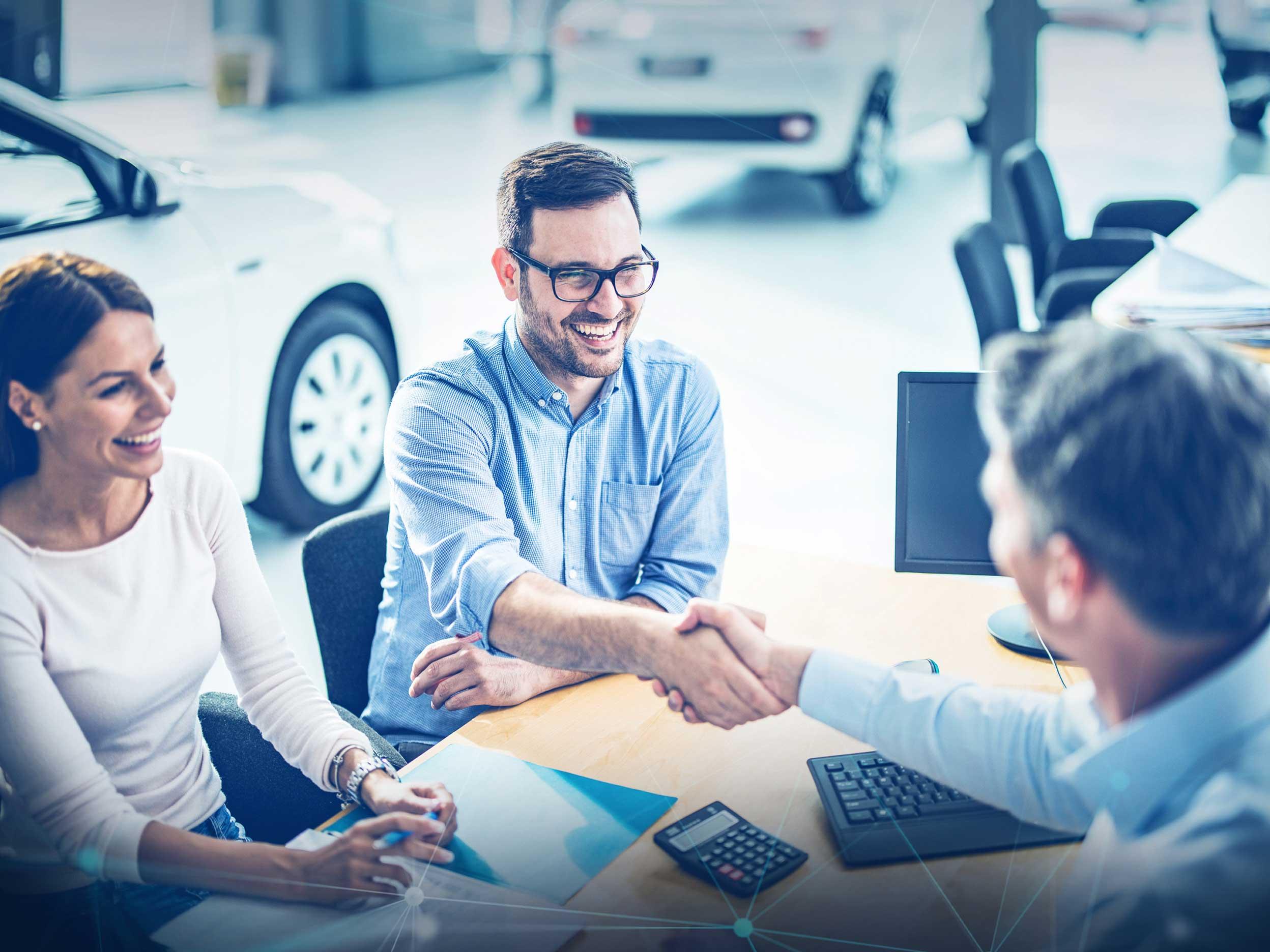 People shaking hands at a desk in car dealership